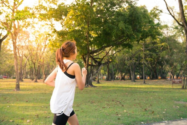 Person jogging outdoors in a green park during sunny weather, wearing athletic gear, promoting fitness, healthy lifestyle, and outdoor exercise.