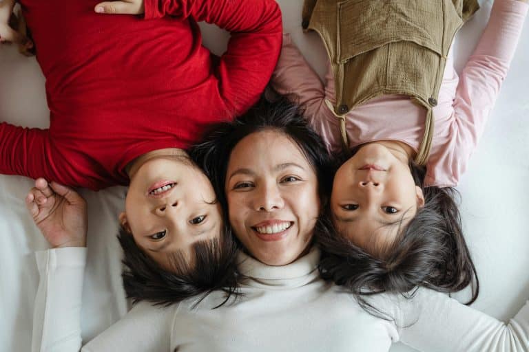 The photo taken from above shows an Asian mother lying on the floor with her two children, whose faces are stuck side by side. The children, a little boy and a little girl, are lying opposite their mother.