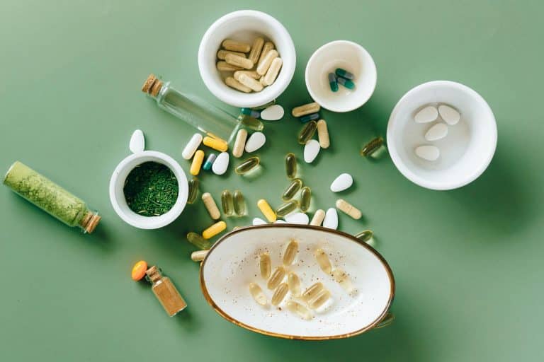 The image features a green background and a view from above of various complementary foods in capsule and pill form, placed on the ground or in bowls. One bowl also contains green tea powder.