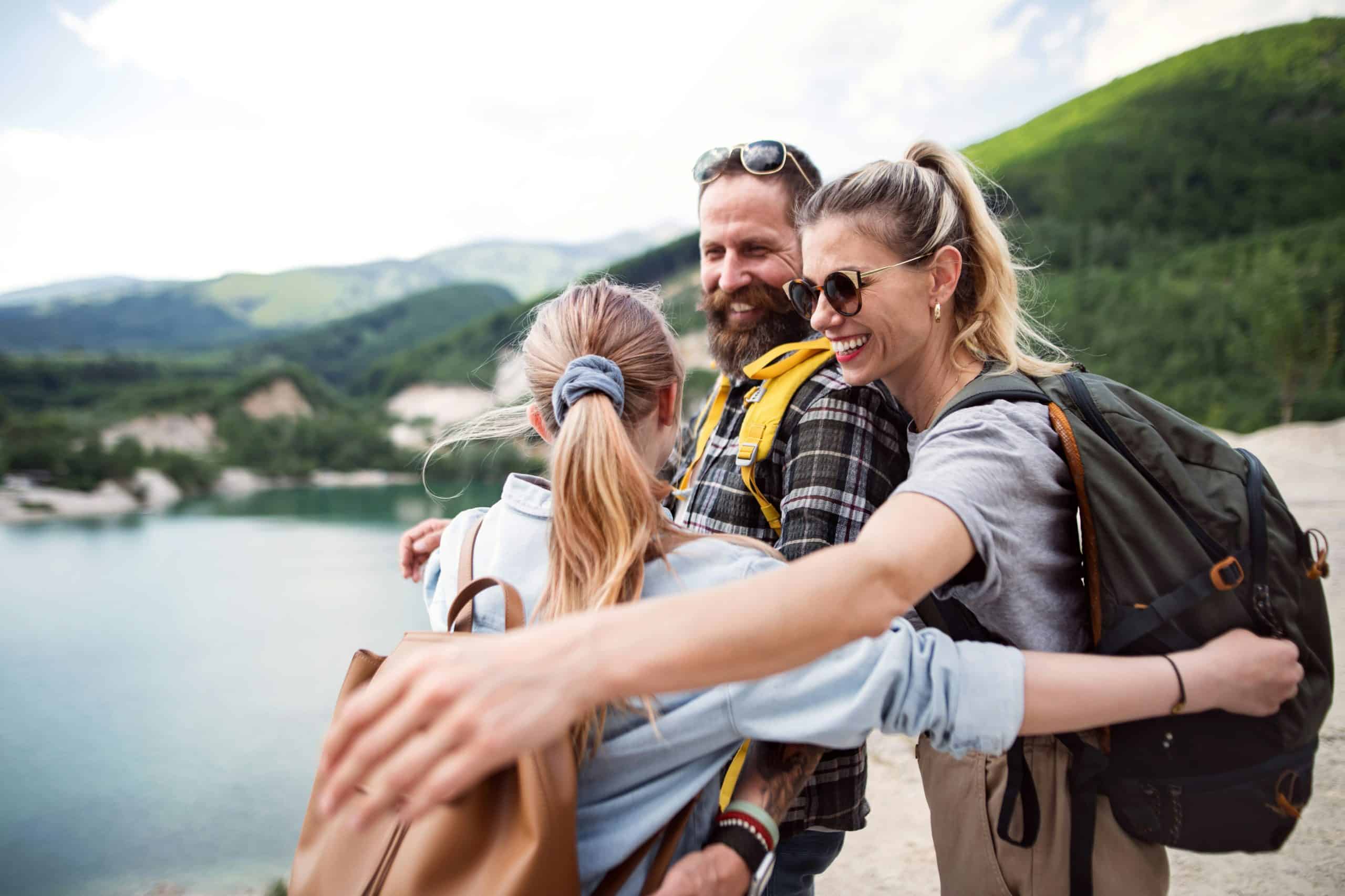 A couple with their daughter hugging in front of a mountain lake during their holiday time.