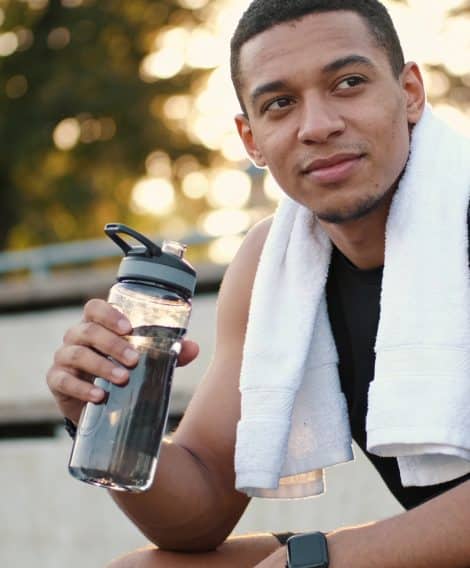 Person sitting outdoors after exercising, holding a water bottle with a towel draped over their shoulders.